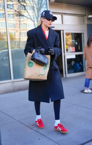 Gigi Hadid styles red trainers with leggings and black coat.